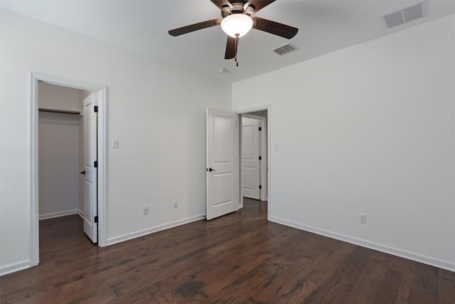 unfurnished bedroom featuring a walk in closet, dark wood-type flooring, a closet, and ceiling fan