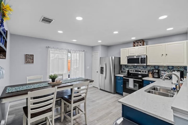 kitchen featuring blue cabinetry, sink, light wood-type flooring, stainless steel appliances, and decorative backsplash