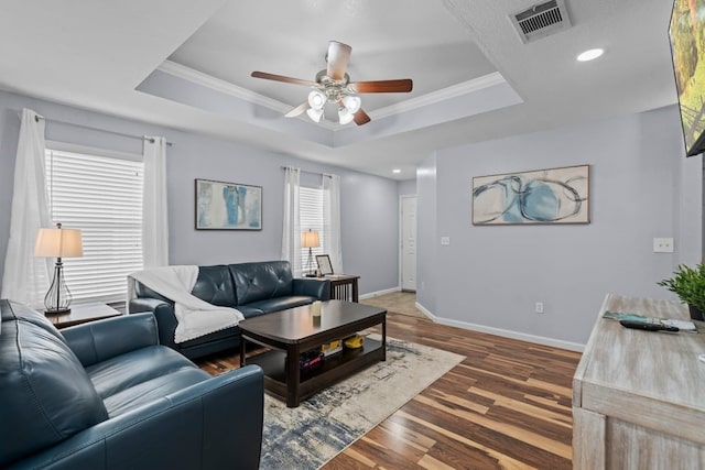 living room featuring crown molding, dark wood-type flooring, a raised ceiling, and ceiling fan