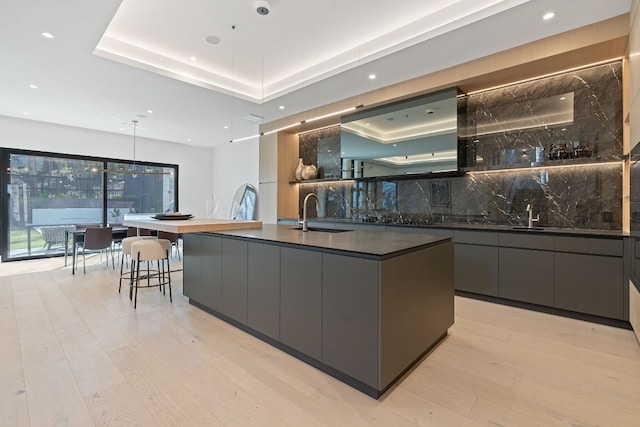 kitchen featuring a raised ceiling, a large island, sink, and decorative light fixtures