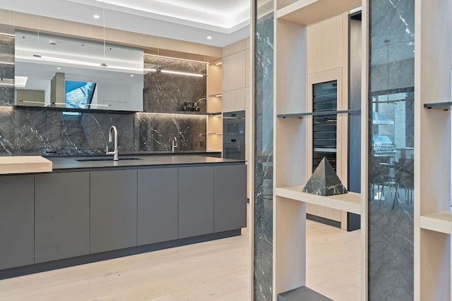 interior space featuring backsplash, light hardwood / wood-style floors, sink, and gray cabinetry