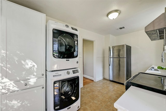 clothes washing area featuring stacked washing maching and dryer, sink, and light tile patterned floors