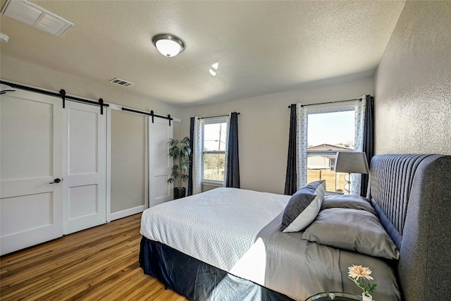 bedroom featuring wood-type flooring, a barn door, and a textured ceiling