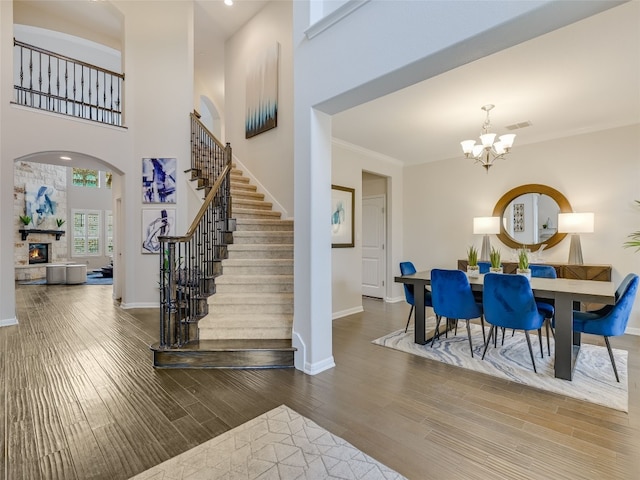 entryway featuring a stone fireplace, an inviting chandelier, crown molding, dark hardwood / wood-style flooring, and a towering ceiling