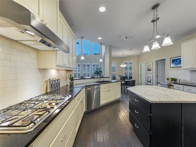 kitchen with dark stone countertops, hanging light fixtures, stainless steel appliances, dark hardwood / wood-style floors, and a kitchen island