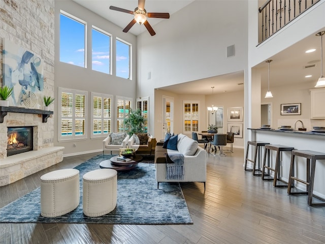 living room featuring hardwood / wood-style flooring, a stone fireplace, ceiling fan with notable chandelier, and a wealth of natural light