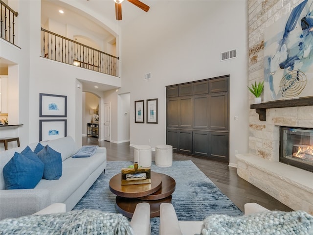 living room featuring ceiling fan, a stone fireplace, and dark hardwood / wood-style flooring