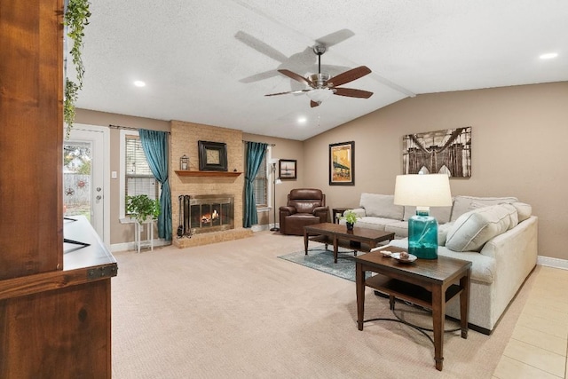 living room featuring lofted ceiling, ceiling fan, a brick fireplace, light carpet, and a textured ceiling