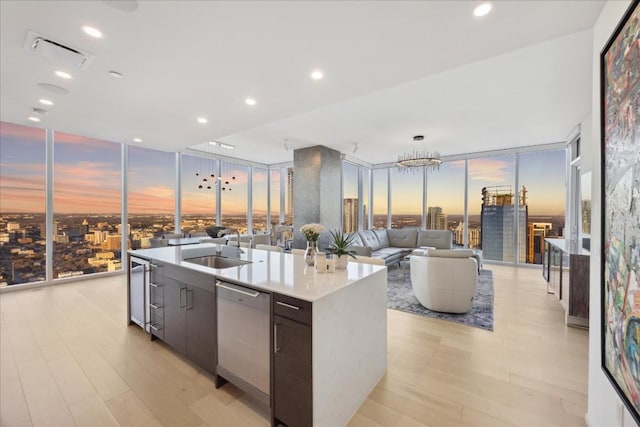 kitchen with sink, dishwashing machine, expansive windows, a center island with sink, and light hardwood / wood-style flooring