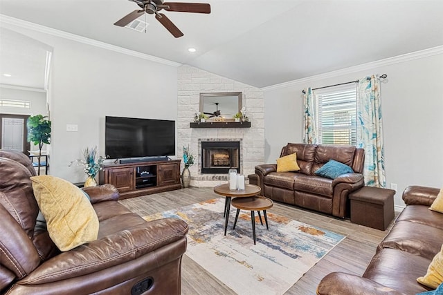 living room with a stone fireplace, vaulted ceiling, light wood-type flooring, ornamental molding, and ceiling fan