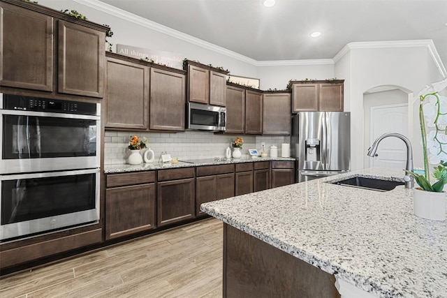 kitchen featuring sink, stainless steel appliances, dark brown cabinetry, ornamental molding, and light stone countertops