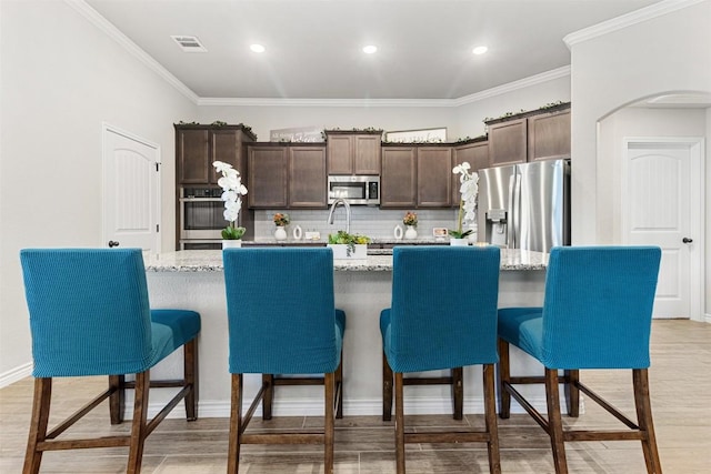 2651 Cowgirl Trl, Belton, TX 76513 - kitchen featuring stainless steel appliances, dark brown cabinetry, decorative backsplash, a large island with sink, and crown molding
