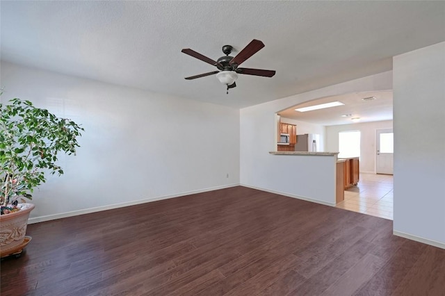 unfurnished living room featuring dark wood-type flooring, ceiling fan, and a textured ceiling