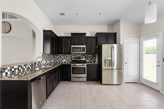 kitchen featuring sink, backsplash, hanging light fixtures, stainless steel appliances, and light stone countertops