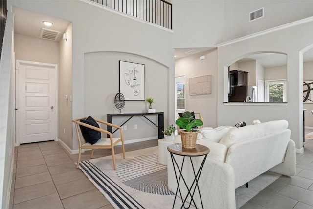 living area with a high ceiling, light tile patterned flooring, baseboards, and visible vents