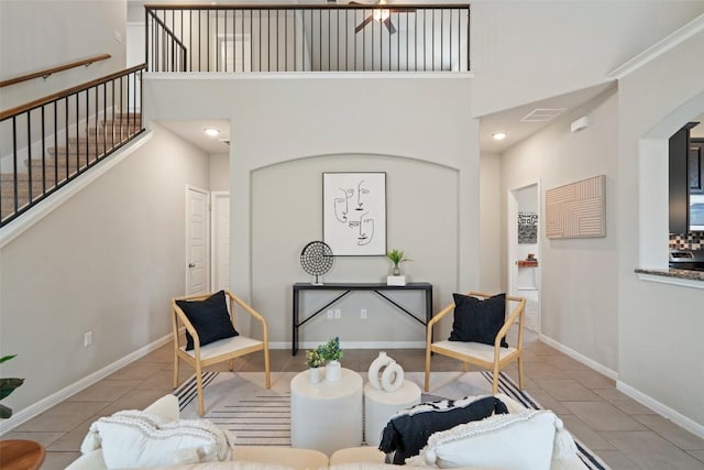 living area with light tile patterned floors, a towering ceiling, baseboards, and stairway