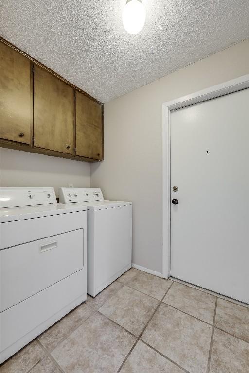 clothes washing area featuring cabinets, light tile patterned floors, a textured ceiling, and independent washer and dryer