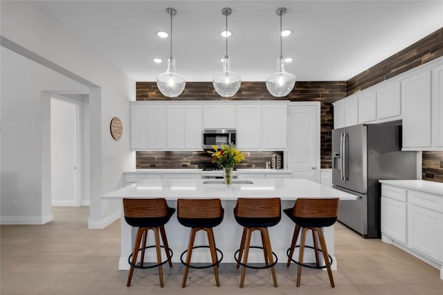 kitchen featuring a kitchen island with sink, hanging light fixtures, backsplash, and appliances with stainless steel finishes