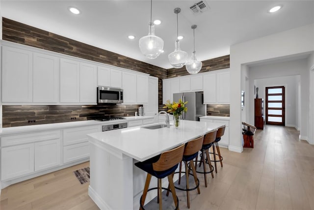 kitchen featuring sink, appliances with stainless steel finishes, white cabinetry, hanging light fixtures, and a center island with sink