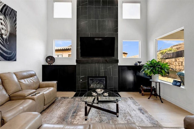 living room with a tile fireplace, a towering ceiling, and light hardwood / wood-style flooring