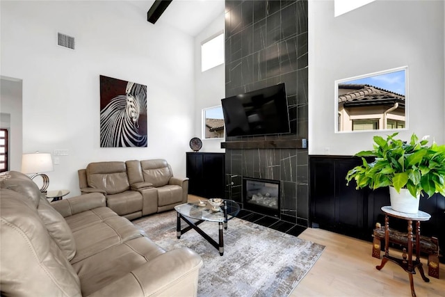 living room with light hardwood / wood-style floors, a tile fireplace, and a high ceiling