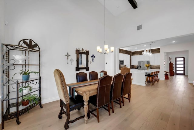 dining space featuring a towering ceiling, a chandelier, and light hardwood / wood-style flooring