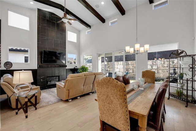 dining room with high vaulted ceiling, light wood-type flooring, beamed ceiling, a fireplace, and ceiling fan with notable chandelier