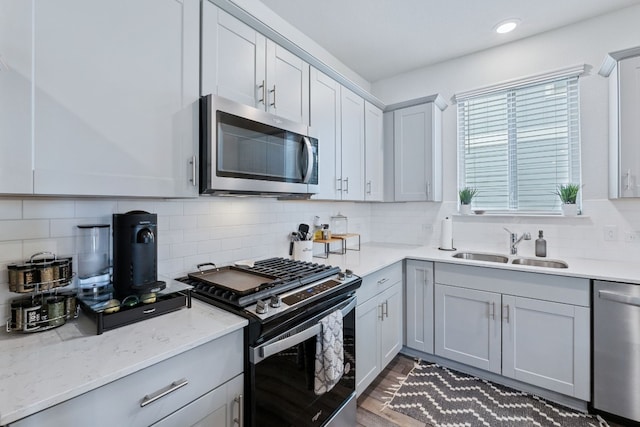 kitchen featuring light stone counters, stainless steel appliances, gray cabinets, backsplash, and a sink