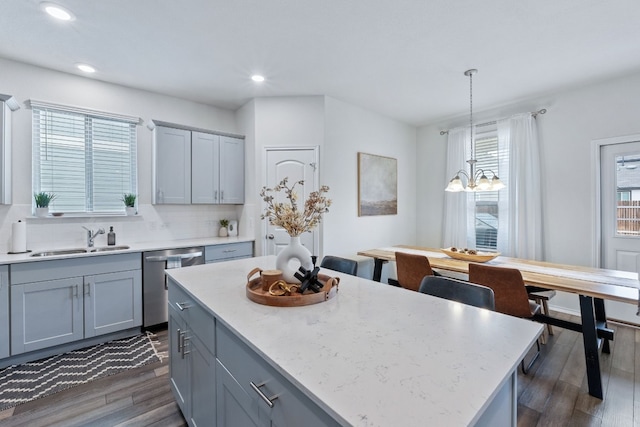 kitchen featuring a center island, decorative light fixtures, dark wood finished floors, stainless steel dishwasher, and a sink