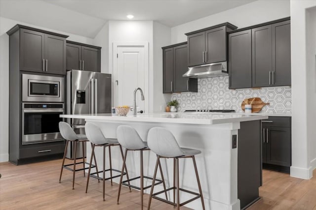 kitchen with stainless steel appliances, tasteful backsplash, a center island with sink, and a kitchen breakfast bar