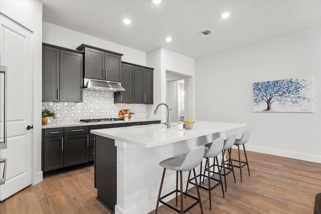 kitchen with tasteful backsplash, a breakfast bar area, a center island with sink, and light hardwood / wood-style floors