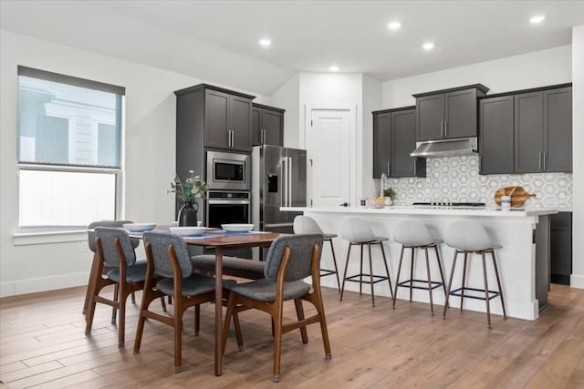 kitchen featuring a breakfast bar area, tasteful backsplash, light hardwood / wood-style flooring, stainless steel appliances, and a kitchen island with sink