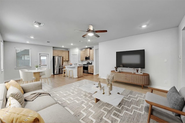 living room featuring sink, ceiling fan, and light wood-type flooring