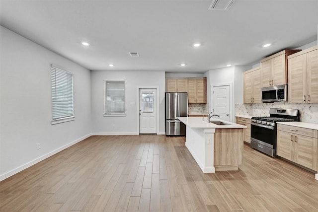 kitchen featuring sink, tasteful backsplash, a center island with sink, light hardwood / wood-style flooring, and stainless steel appliances