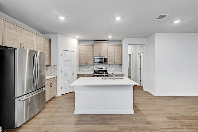 kitchen featuring light countertops, a sink, light wood-style floors, decorative backsplash, and appliances with stainless steel finishes