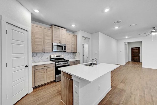 kitchen featuring a kitchen island with sink, sink, stainless steel appliances, and light brown cabinets