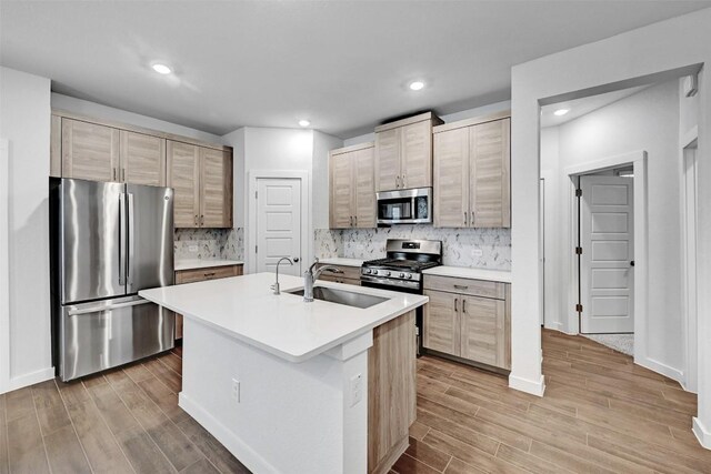 kitchen featuring sink, light hardwood / wood-style flooring, backsplash, stainless steel appliances, and an island with sink