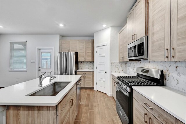 kitchen with stainless steel appliances, sink, a center island with sink, and light brown cabinets