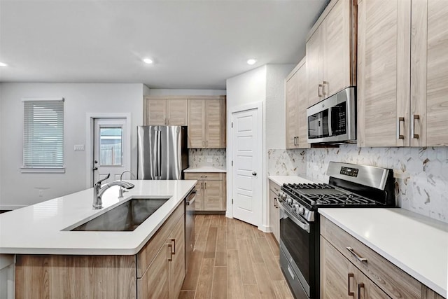 kitchen with stainless steel appliances, sink, an island with sink, and light brown cabinets