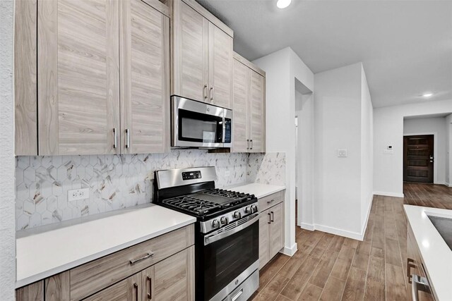 kitchen featuring stainless steel appliances, light wood-type flooring, backsplash, and light brown cabinetry