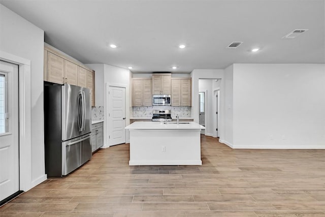 kitchen with stainless steel appliances, tasteful backsplash, a kitchen island with sink, and light brown cabinetry