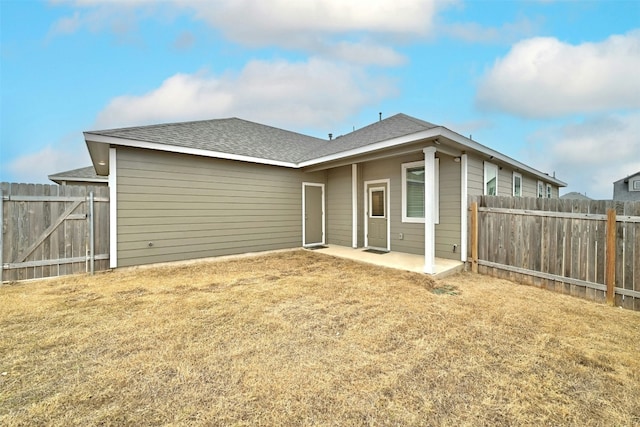 back of house with a fenced backyard, roof with shingles, a patio area, and a lawn
