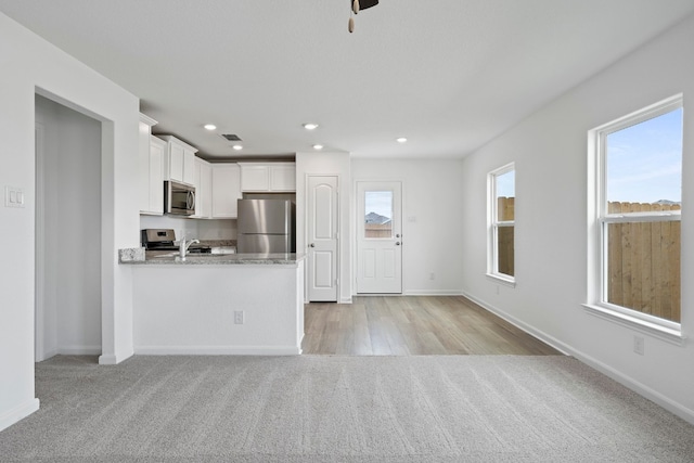 kitchen with white cabinetry, appliances with stainless steel finishes, light colored carpet, and light stone counters