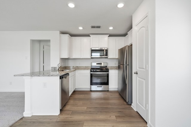 kitchen featuring white cabinetry, kitchen peninsula, stainless steel appliances, light stone countertops, and light hardwood / wood-style floors