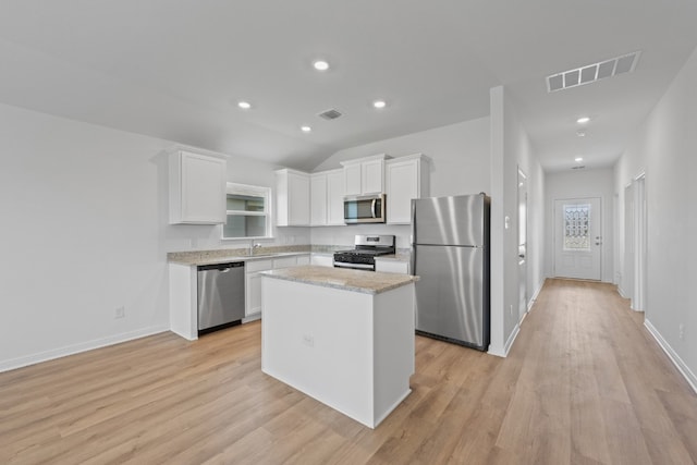 kitchen with light wood-type flooring, stainless steel appliances, white cabinets, and a kitchen island