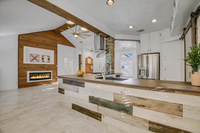 kitchen with white cabinetry, sink, stainless steel fridge with ice dispenser, a barn door, and wall chimney range hood