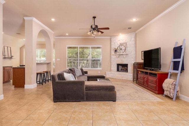 living room featuring light tile patterned floors, crown molding, a stone fireplace, and ceiling fan