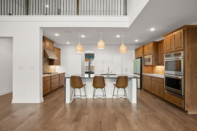 kitchen with appliances with stainless steel finishes, decorative light fixtures, a kitchen bar, hardwood / wood-style flooring, and a kitchen island with sink