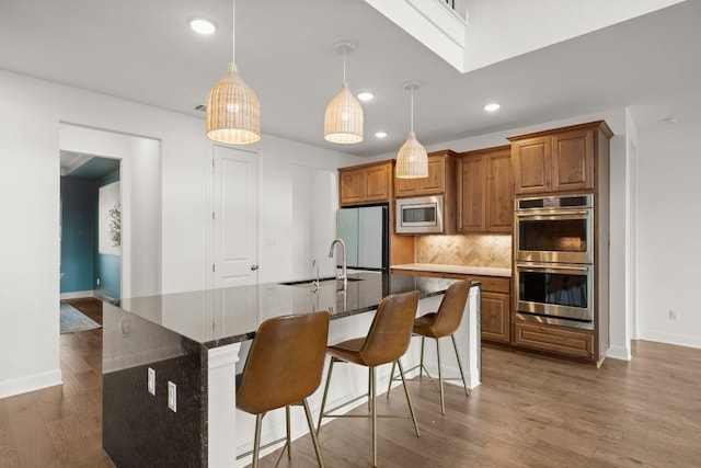 kitchen with sink, decorative light fixtures, stainless steel appliances, and an island with sink