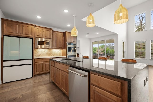 kitchen featuring sink, dark stone countertops, hanging light fixtures, stainless steel appliances, and a center island with sink